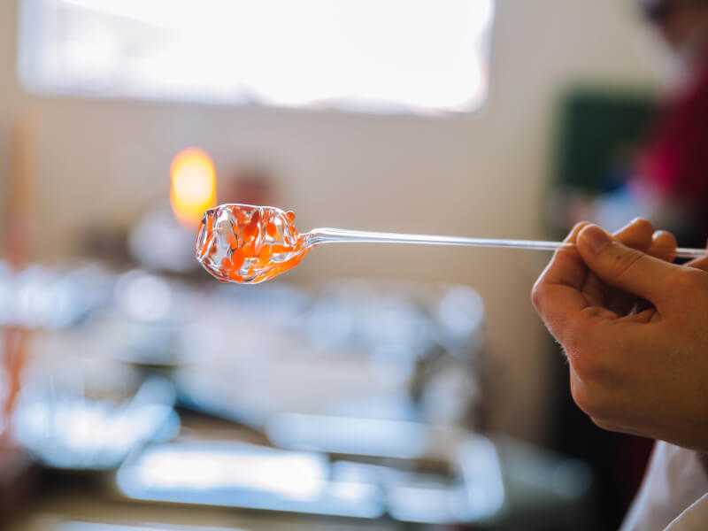 Hand holding a molten glass-blown object on a rod